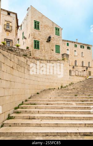 Escalier en pierre menant à des bâtiments européens traditionnels avec volets verts sous un ciel nuageux, Sibenik, Croatie Banque D'Images