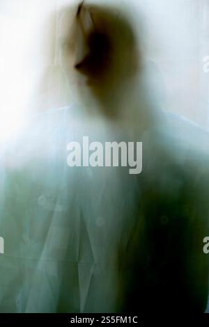 Silhouette floue d'une personne derrière un rideau blanc présentant un aspect abstrait et éthéré. Banque D'Images
