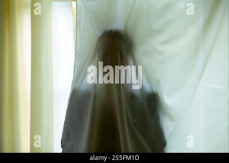 Silhouette floue d'une personne derrière des rideaux blancs présentant un aspect abstrait et éthéré. Banque D'Images