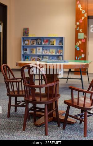 Chaises en bois entourant une table dans une bibliothèque avec étagères et décoration murale alphabet pour enfants en arrière-plan. Cleveland, Ohio, États-Unis Banque D'Images