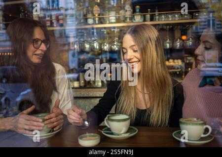 Trois femmes apprécient une conversation autour d'un café à l'intérieur d'un café confortable, avec un reflet visible de la rue dans la fenêtre, Berlin, Allemagne Banque D'Images