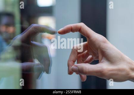 Gros plan de la main d'une personne qui tend la main pour toucher une surface en verre avec un reflet visible, Berlin, Allemagne Banque D'Images