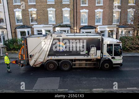 Camion de collecte des ordures avec poubelle ou collecteur de déchets derrière et slogan sur le côté disant gaspiller les aliments alimente le changement climatique. Maisons derrière. Holloway Banque D'Images