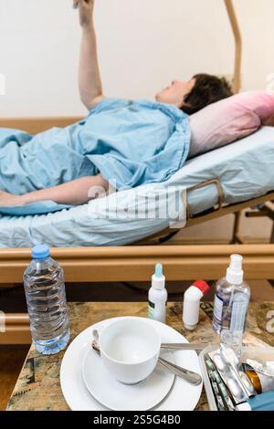tasse blanche avec soucoupe et médicaments sur table et femme malade tenant la poignée du lit d'hôpital de soins à domicile sur le fond à la maison Banque D'Images
