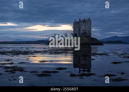 Le château historique de Castle Stalker se trouve dans le loch marin de Loch Laich dans les Highlands de l'Ouest écossais alors que le soleil se couche en arrière-plan, Banque D'Images