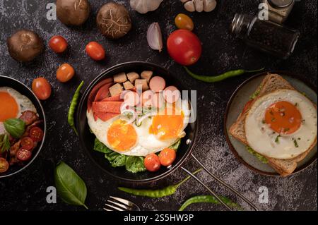 Petit déjeuner avec œufs au plat, saucisses et jambon dans une poêle avec tomates. Chili et basilic. Banque D'Images