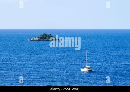 yacht catamaran naviguant vers une petite île inhabitée solitaire dans la mer, concept d'un bateau, une île inhabitée et une mer bleue à l'horizon Banque D'Images