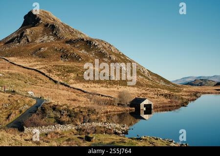 Une maison de bateau se trouve au bord des lacs de Cregennan, ou Llynnau Cregennan, près d'Arthog, Dolgellau, au nord du pays de Galles avec la crête de Pared y Cefn hîr au-dessus Banque D'Images