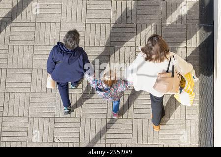 Famille marchant ensemble à l'extérieur, les parents tenant la main de leur fille sur un trottoir carrelé, vu d'en haut Banque D'Images