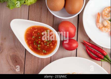 Trois crevettes fraîches, œufs, Chili, sauce et demi-tomates dans une assiette blanche sur un bois. Banque D'Images