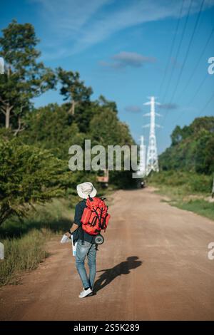 Vue arrière du jeune voyageur homme avec sac à dos portant sombrero et tenant la carte en papier à la main, il marche et regarde vers l'avant, a le pôle haute tension et Banque D'Images
