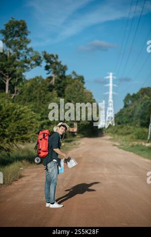Vue arrière du jeune voyageur homme avec sac à dos portant sombrero et tenant la carte en papier à la main, il marche et regarde vers l'avant, a le pôle haute tension et Banque D'Images
