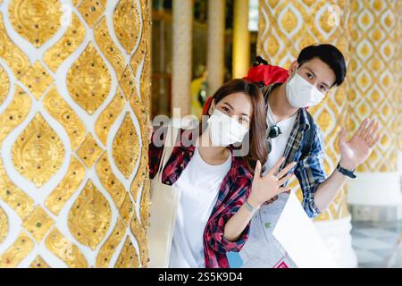 Portrait jeune couple de routards asiatiques debout et tiennent la carte de papier à la main au beau temple thaïlandais, ils agitent la main à saluer et regarder Banque D'Images