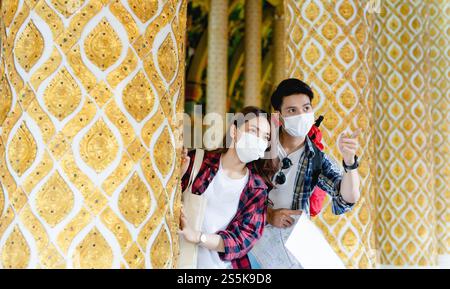 Portrait jeune couple de routards asiatiques debout et tenir la carte de papier à la main au beau temple thaïlandais, bel homme pointant et ils regardent Banque D'Images