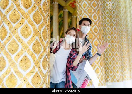 Portrait jeune couple de routards asiatiques debout et tiennent la carte de papier à la main au beau temple thaïlandais, ils agitent la main à la salutation et regardent vers l'avant Banque D'Images
