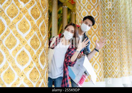 Portrait jeune couple de routards asiatiques debout et tiennent la carte de papier à la main au beau temple thaïlandais, ils agitent la main à saluer et regarder Banque D'Images