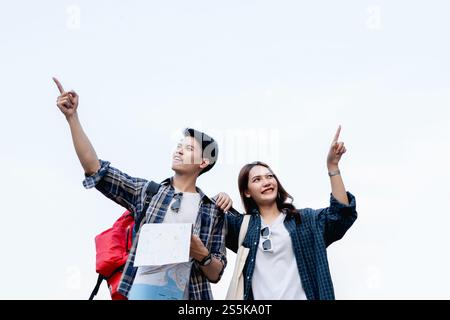 Portrait joyeusement jeune couple de routards sourire et pointant les doigts dans différentes directions tout en voyageant sur la ville de rue, bel homme tenant Banque D'Images
