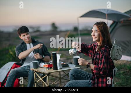 Joyeux couple jeune routard assis à l'avant de la tente dans la forêt avec set à café et faire moulin à café frais pendant le voyage de camping en été Banque D'Images