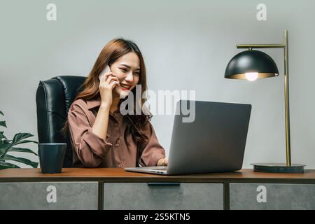 Heureusement jeune femme asiatique avec une nouvelle normalité, elle reste à la maison et travaille de la maison, parlant sur le téléphone mobile et utiliser un ordinateur portable pendant Banque D'Images