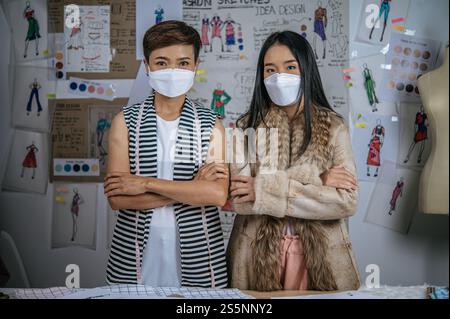 Portrait jeune femme asiatique et ami debout avec des bras croisés ensemble dans un atelier moderne. Des femmes positives collaboratrices créatives portant des mas de visage médical Banque D'Images