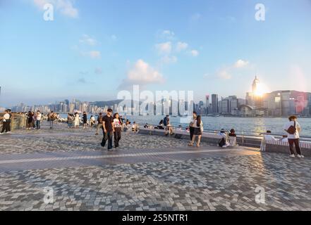 Hong Kong - 17 novembre 2024 : Une journée ensoleillée sur une promenade au bord de l'eau. Les gens se promènent le long de la passerelle pavée, en profitant de la vue sur le paysage urbain à travers la W. Banque D'Images
