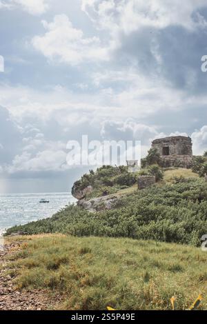 Prises à Tulum, au Mexique, les ruines mayas avec un temple en pierre se trouvent au sommet d'une colline herbeuse surplombant la mer des Caraïbes. Il y a un bateau dans l'eau Banque D'Images