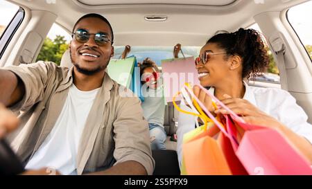 Happy Black Family assis tenant les sacs à provisions dans la voiture Banque D'Images