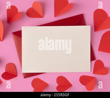 Papier blanc et coeurs rouges sont placés sur un fond rose. Banque D'Images