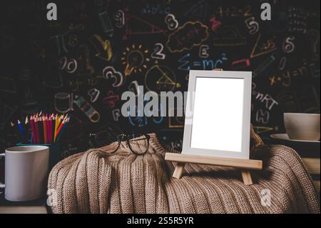 cadre photo blanc sur le stand et lunettes sur le pull en classe avec tasse et crayons de couleur. Banque D'Images