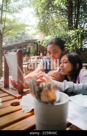 Mère d'Asie du Sud-est et fille adolescente regardant le menu, discutant et choisissant pour les repas au restaurant en plein air Banque D'Images