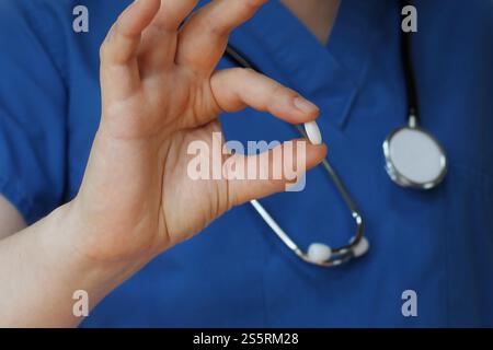 Gros plan professionnel médical dans les gommages bleus tenant la pilule blanche, les médicaments Banque D'Images