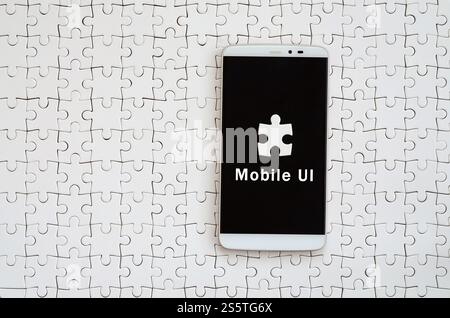 Un smartphone moderne avec un écran tactile se trouve sur un casse-tête blanche dans un état assemblé avec l'inscription. Interface utilisateur mobile Banque D'Images