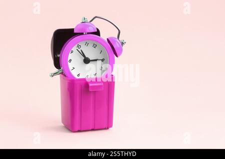 Concept de perte de temps. Réveils roses dans une poubelle en plastique sur fond pêche. Mauvaise et mauvaise gestion du temps. Concept de perte de temps. Réveil en entrée Banque D'Images