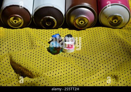 Plusieurs casquettes pour pulvérisateurs de peinture aérosol usagés reposent sur le maillot de sport d'un joueur de basket-ball en tissu polyester. Le concept de rue de la jeunesse Banque D'Images