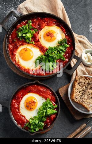 Oeufs Shakshuka dans une casserole avec du pain sur un fond sombre. Oeufs pochés dans une sauce épicée au poivre tomate. Œufs brouillés juifs traditionnels. Vue de dessus. Banque D'Images