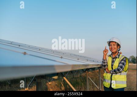 Portrait asiatique jeune belle femme dans un casque de protection. Ingénieur féminin avec détermination au panneau solaire à l'extérieur. croiser les bras et regarder Banque D'Images