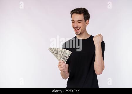 Portrait d'un homme joyeux tenant des billets d'un dollar et faisant un geste gagnant serrant le poing sur fond blanc. Finance, investissement et économies Banque D'Images