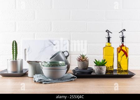 Ustensiles de cuisine en céramique sur le comptoir en bois, huile dans des bouteilles pour la cuisson. Plantes. Vue de face. Mur de briques blanches. Style moderne de l'espace cuisine. Banque D'Images