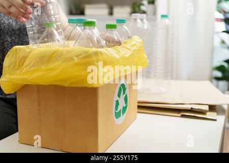 Accueil recycler ECO vert zéro concept Femme jetant bouteille en plastique vide dans le bac de recyclage avec sacs à ordures jaunes à la maison Banque D'Images