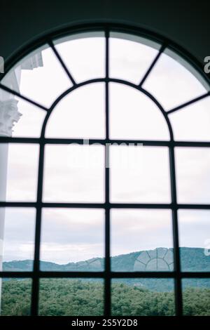 Vue sur les collines verdoyantes à travers une grande fenêtre cintrée, offrant une évasion paisible. Banque D'Images