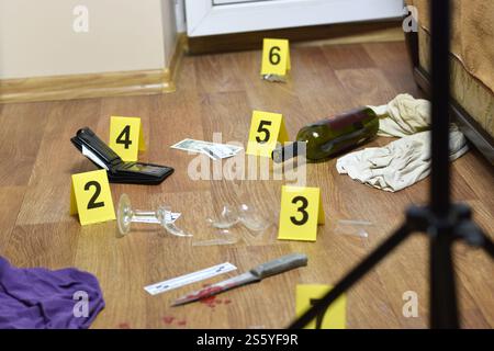 Enquête sur les lieux du crime - numérotation des preuves après le meurtre dans l'appartement. Verre cassé de vin, couteau avec des vêtements, portefeuille et bouteille comme Banque D'Images