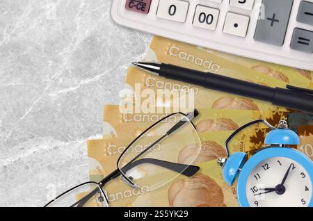 Billets de 100 dollars canadiens et calculatrice avec lunettes et stylo. Concept de prêt commercial ou de saison de paiement d'impôt. Planification financière et délai de paiement Banque D'Images