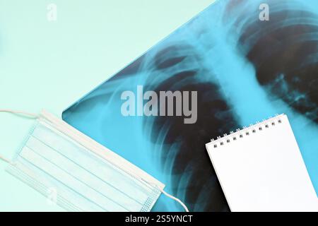 Masque respiratoire et page de bloc-notes vide sur la radiographie des poumons humains, vue de dessus. Concept de pneumonie à coronavirus COVID-19. Masque respiratoire et bloc-notes vide Banque D'Images