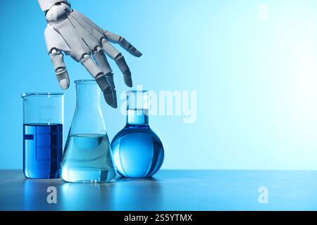 Intelligence artificielle. Main de robot et verrerie de laboratoire avec des liquides sur la table sur fond bleu clair, espace pour le texte Banque D'Images