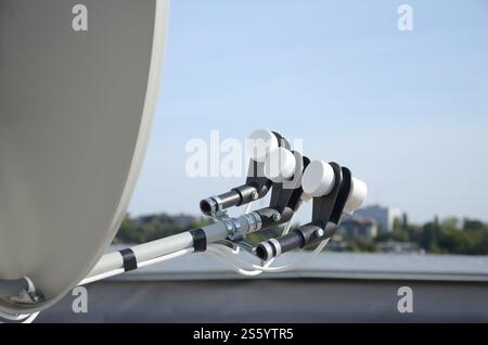 Antenne parabolique blanche avec trois convertisseurs montés sur le mur en béton du toit d'un bâtiment résidentiel. Publicité télévisée par satellite. Satellite blanc Banque D'Images