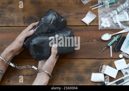 Trafiquant de drogue arrêté avec leurs paquets d'héroïne. La police arrête le trafiquant de drogue avec des menottes et beaucoup de stupéfiants sur la table en bois. 26 juin Banque D'Images
