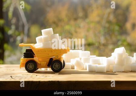 Un petit camion-jouet jaune est chargé de cubes de sucre blanc près des débris de sucre. Une voiture sur une surface en bois sur un fond de forêt d'automne. Banque D'Images