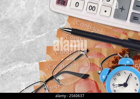 Billets de 50 dollars canadiens et calculatrice avec lunettes et stylo. Concept de prêt commercial ou de saison de paiement d'impôt. Planification financière et temps pour payer les impôts. Banque D'Images