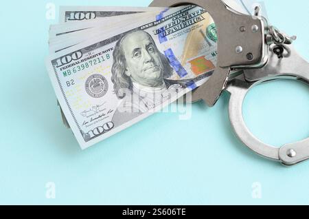 Menottes de police argentées et billets de cent dollars se trouvent sur fond bleu clair. Menottes de police argentées et billets de cent dollars gisent sur bleu clair Banque D'Images