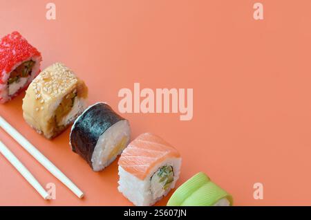 Différents types de rouleaux de sushi asiatiques sur fond orange gros plan. Minimalisme vue de dessus plat avec de la nourriture japonaise. Différents types de sushis asiatiques Banque D'Images